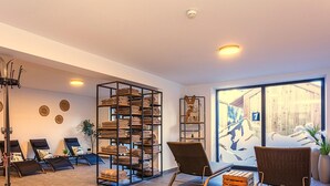 A spacious room with a large window, a metal shelf with towels, two wicker chairs, and a massage chair. - Ski-in, ski-out in Alpine style and sauna (Hinterglemm)