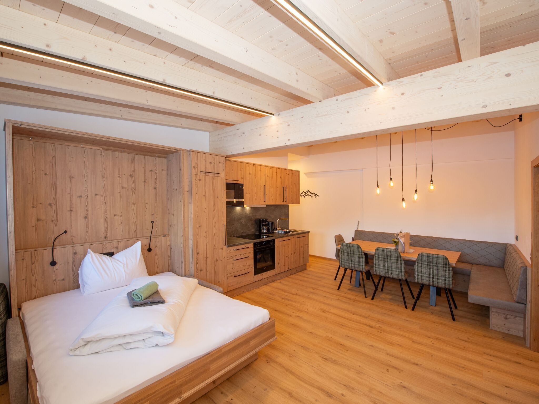 A modern bedroom with a wooden bed, a kitchenette, and a dining area with a sofa and chairs.