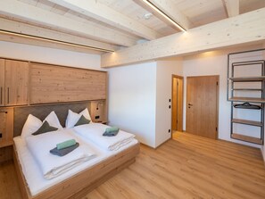 A bedroom with a wooden bed, a wardrobe, and a door leading to another room. - Ski-in, ski-out in Alpine style and sauna (Hinterglemm)