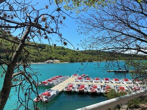 Ein Yachthafen mit vertäuten Booten, eine Holzsteganlage und im Hintergrund ein klarblauer See sowie grüne Hügel.