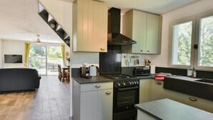A modern kitchen with a built-in stove, oven, and microwave. There is a dining area with a table and chairs, and a staircase leading to an upper level. - Lovely little house for two nestled in nature (Flayosc)