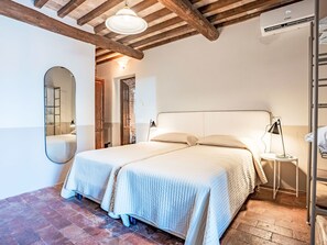 A double bed with a headboard, a bedside table with a lamp, a mirror, and a wooden ceiling with exposed beams. - Apartment Ulivo by Interhome (Grosseto)