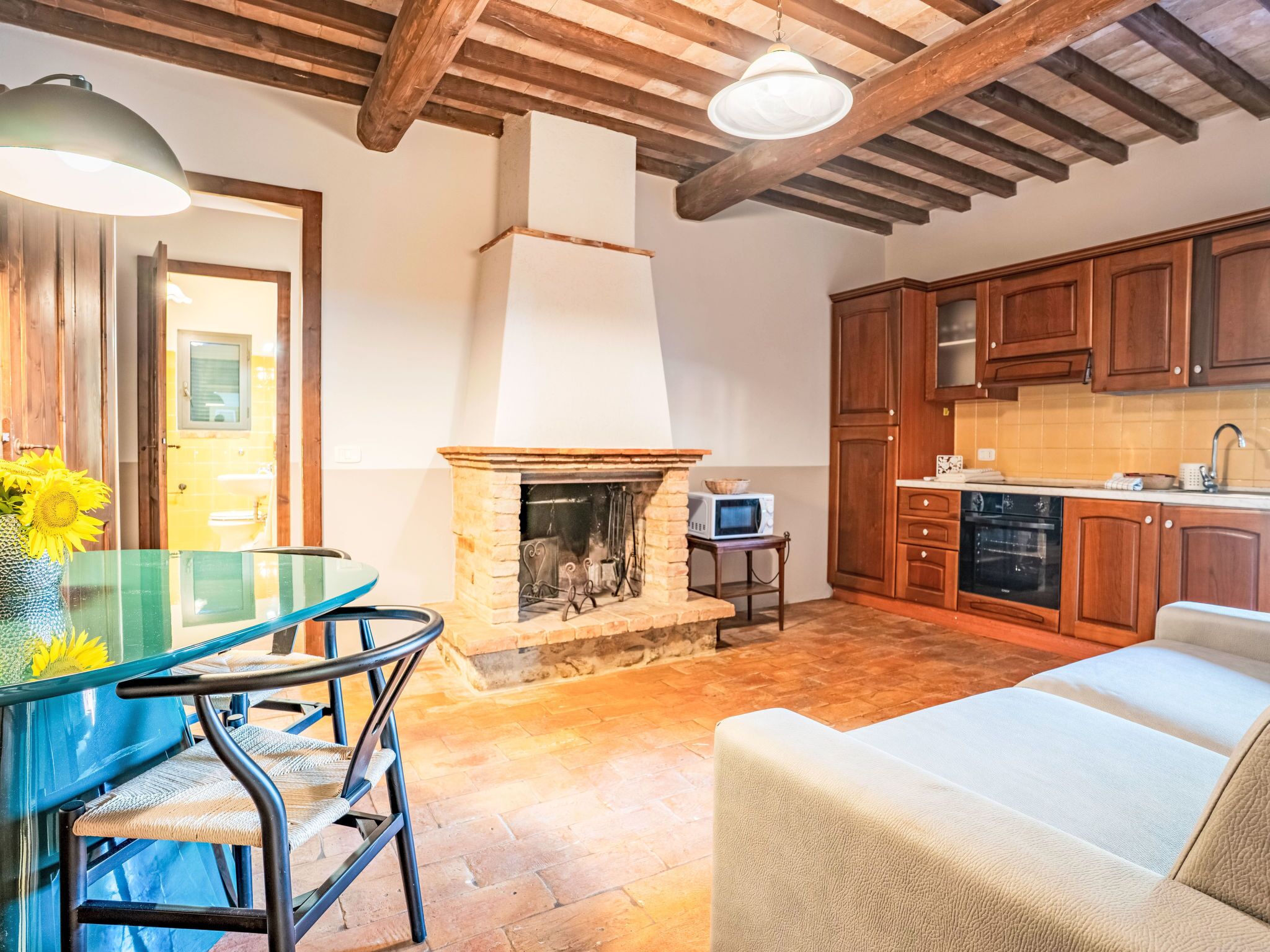 A cozy kitchen with wooden cabinets, a stone fireplace, and a dining area with a glass table and chairs.