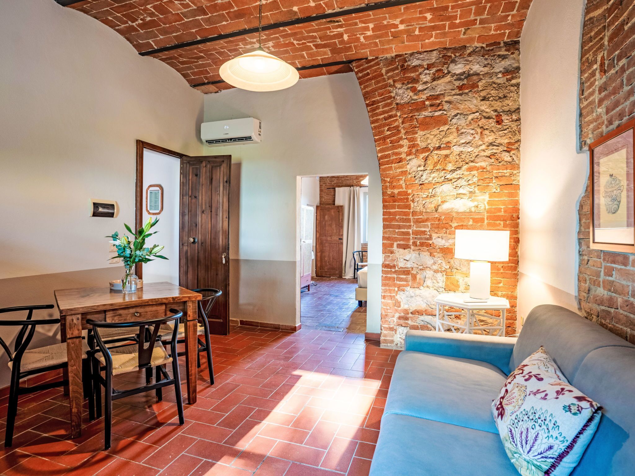 A cozy living area with a brick wall, a dining table with chairs, a sofa, and a lamp.