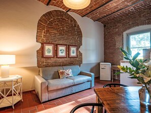 A cozy living area with a brick wall, a sofa, a small table with a lamp, a refrigerator, and a window with natural light. - Apartment Madia by Interhome (Grosseto)
