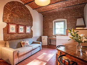 A cozy living room with a brick wall, a sofa, a small table with a vase, and a window. - Apartment Madia by Interhome (Grosseto)