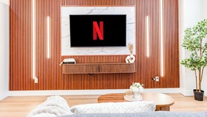 A modern living room with a TV mounted on a wooden wall, a small shelf with books, and a potted plant. - Entire Spacious Luxury Retreat Near DT | Sleeps 4 | Fast Wifi | Free Parking (Calgary)