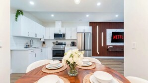 A modern kitchen with white cabinets, stainless steel appliances, and a wooden dining table set with white plates and a vase of flowers. - Entire Spacious Luxury Retreat Near DT | Sleeps 4 | Fast Wifi | Free Parking (Calgary)