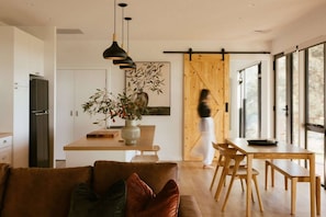Une cuisine moderne dotée d’une porte coulissante en bois, un coin repas avec une table et des chaises en bois, et un salon avec un canapé.
