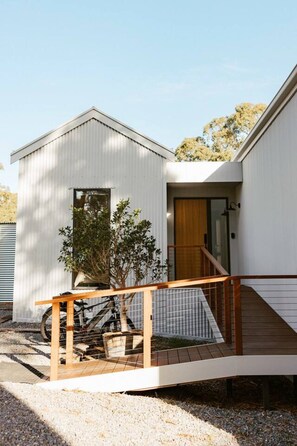 A modern single-story house with a wooden staircase leading to a front door, a small porch area, and a bicycle parked outside. - Escape One - Luxury vineyard escape (McLaren Vale)