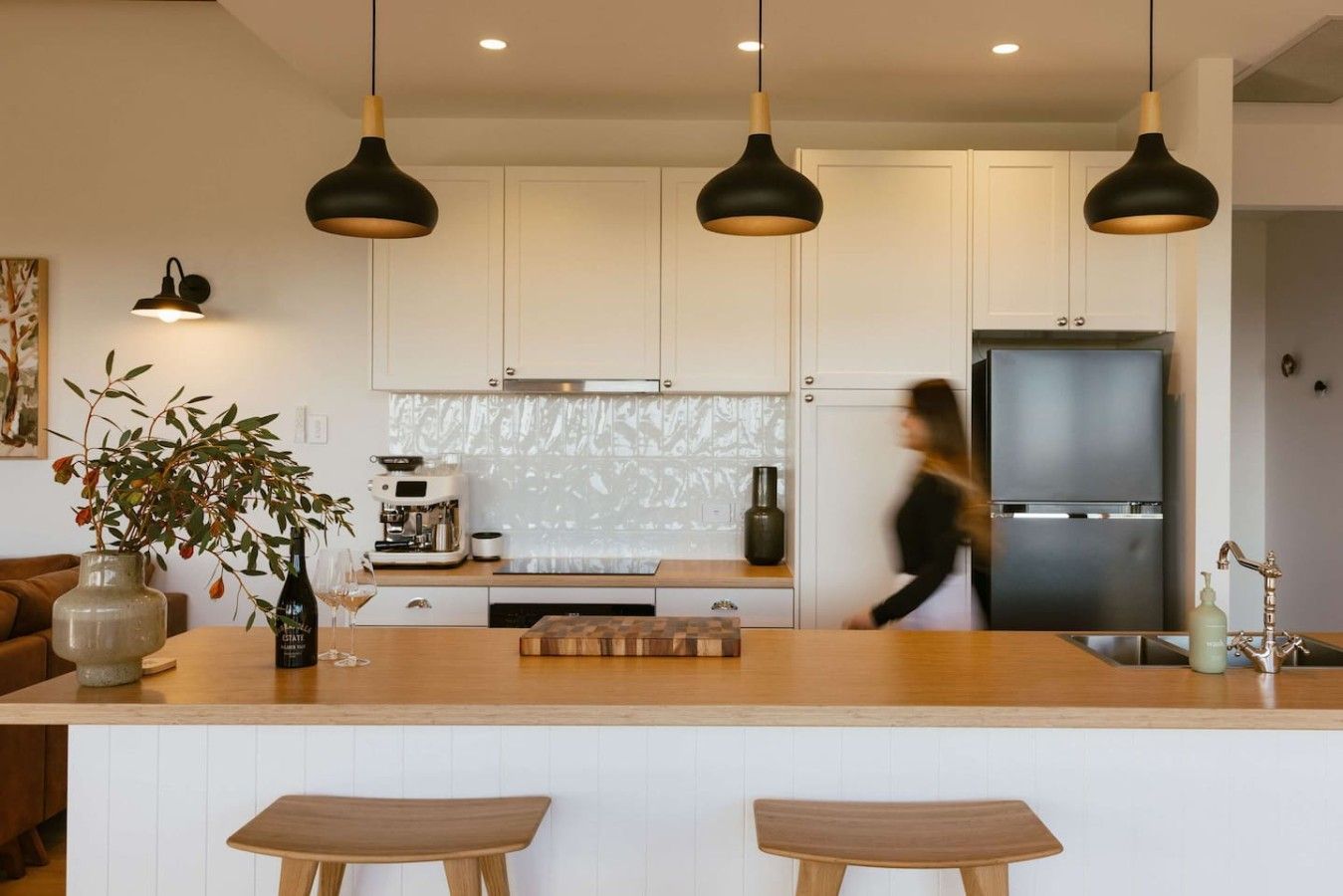 A modern kitchen with white cabinets, a central island with stools, pendant lighting, and a stainless steel refrigerator.