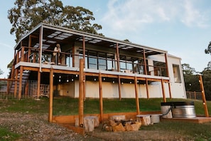 A modern two-story house with a large balcony, wooden deck, and a fire pit area.