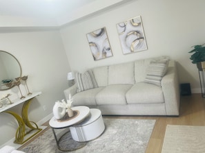 Ein Wohnzimmer mit einer Couch, einem runden Couchtisch, einem Spiegel und abstrakter Kunst an der Wand.