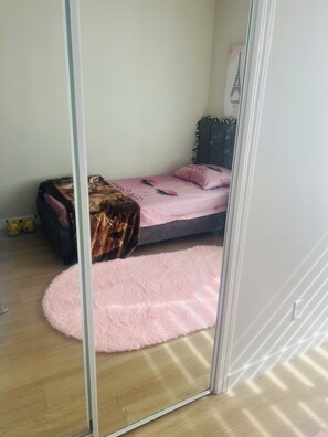 Ein Schlafzimmer mit einem Bett, einem flauschigen rosa Teppich, einem Kleiderschrank und einem Pikachu Kuscheltier auf dem Boden.