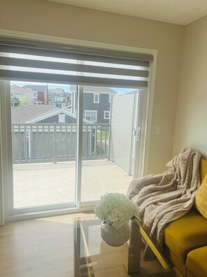 A room with a yellow sofa, a white vase with flowers, and a sliding glass door leading to a balcony. - Beautiful, Modren family house 5 min from airport near busstop,resturants,Malls (Calgary)
