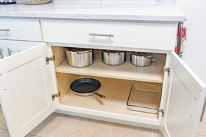 A kitchen cabinet with three stainless steel pots, a frying pan, and a clear plastic container. - Vancouver Verdant Villa (Vancouver)