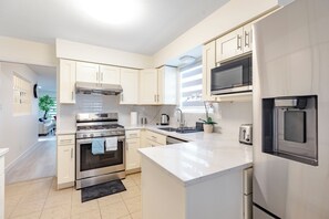 A modern kitchen with stainless steel appliances, white cabinetry, and a large island. - Vancouver Verdant Villa (Vancouver)