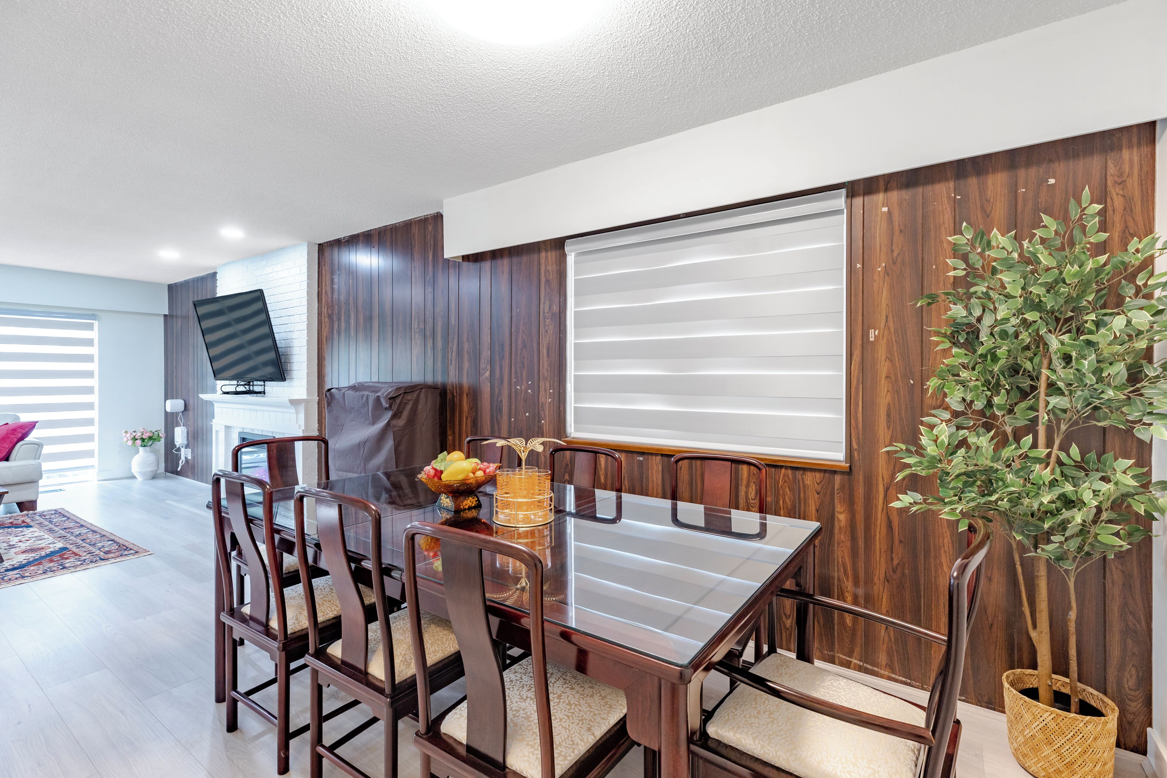 A dining area with a wooden table and chairs, a television, and a potted plant.