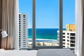 A hotel room with a large window overlooking a beach and ocean, a bed, and a lamp. - [SEA BREEZE] North East Ocean View Studio @ Mantra Legends (Surfers Paradise)