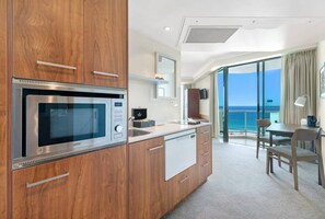 A modern kitchen with a built-in microwave, wooden cabinets, and a view of the ocean through large windows. - [SEA BREEZE] North East Ocean View Studio @ Mantra Legends (Surfers Paradise)