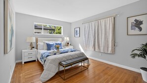 Un dormitorio con cama, mesitas de noche, una ventana, un banco y una planta en maceta.