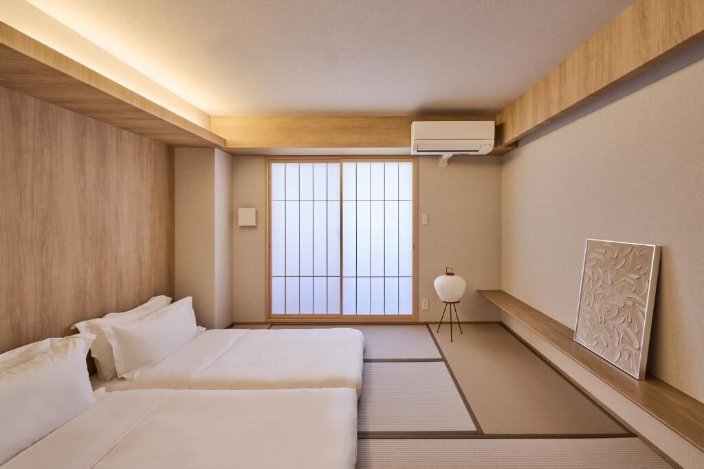Camera d'albergo con due letti, una porta scorrevole in stile shoji, un piccolo tavolino rotondo e un condizionatore d'aria a parete.