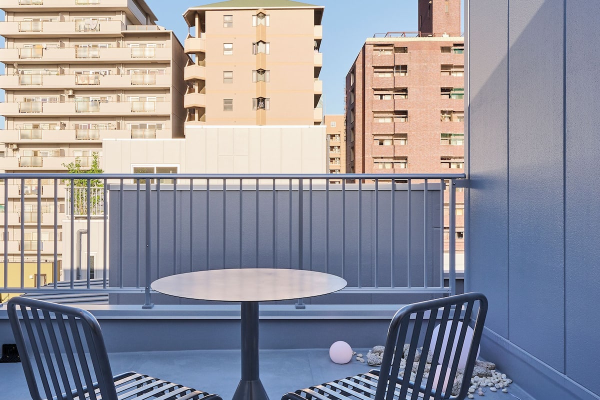 A balcony with a round table and two chairs, overlooking a cityscape with buildings.