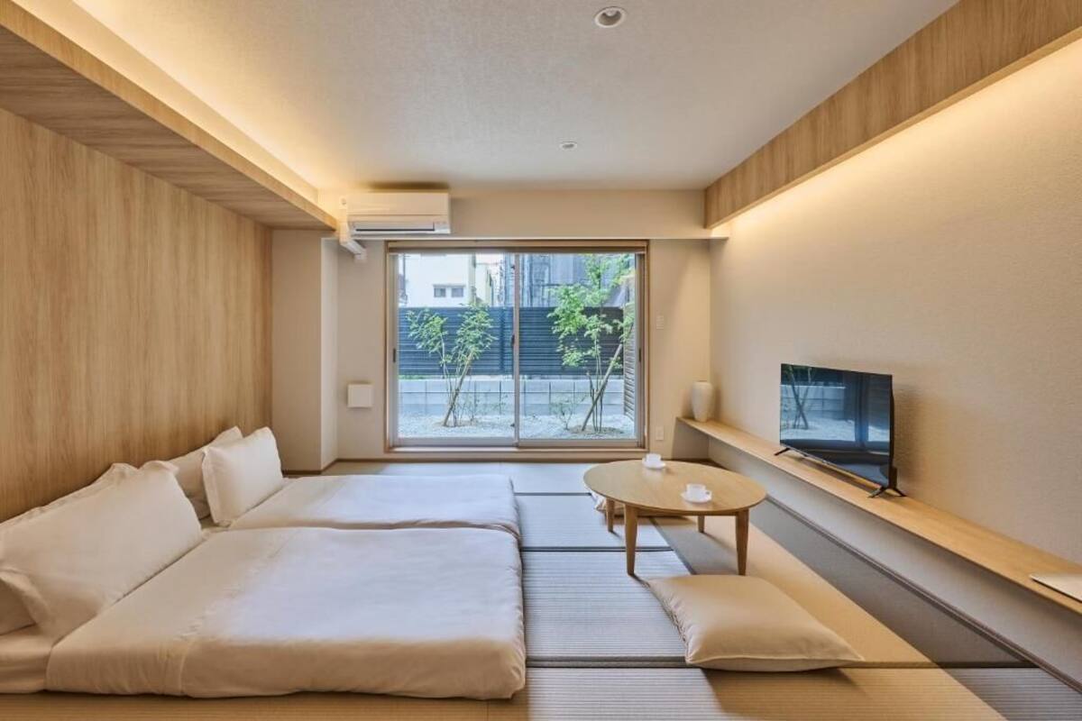 A modern hotel room with a sofa bed, a small table, a TV, and a view of the outside.