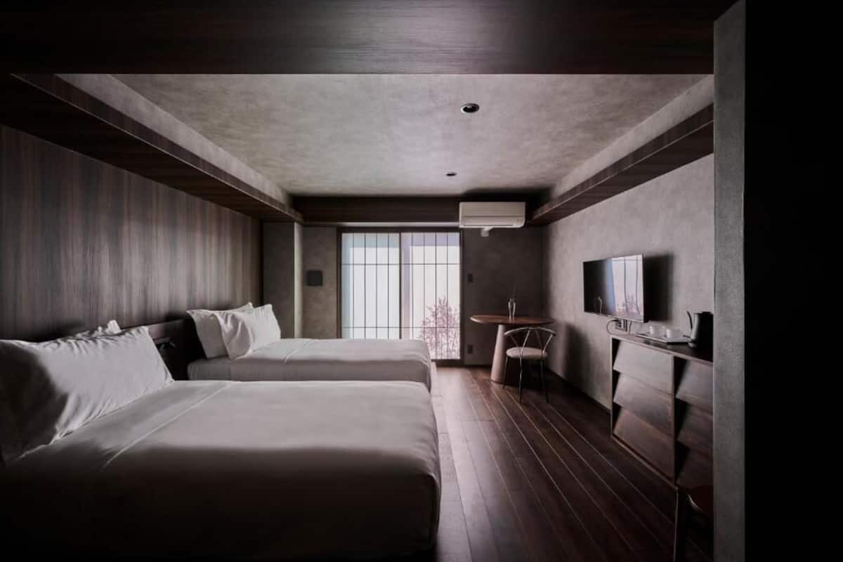 A hotel room with two beds, a TV, a desk, and a window with a view.