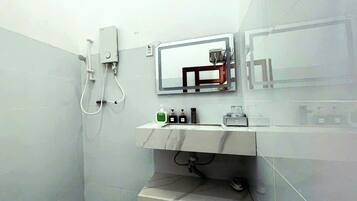 Een badkamer met een douche, een wastafel met toiletartikelen en een spiegel.
