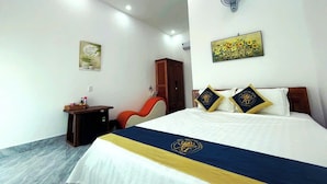 Habitación de hotel con cama, escritorio, silla, armario, ventilador y un cuadro en la pared.