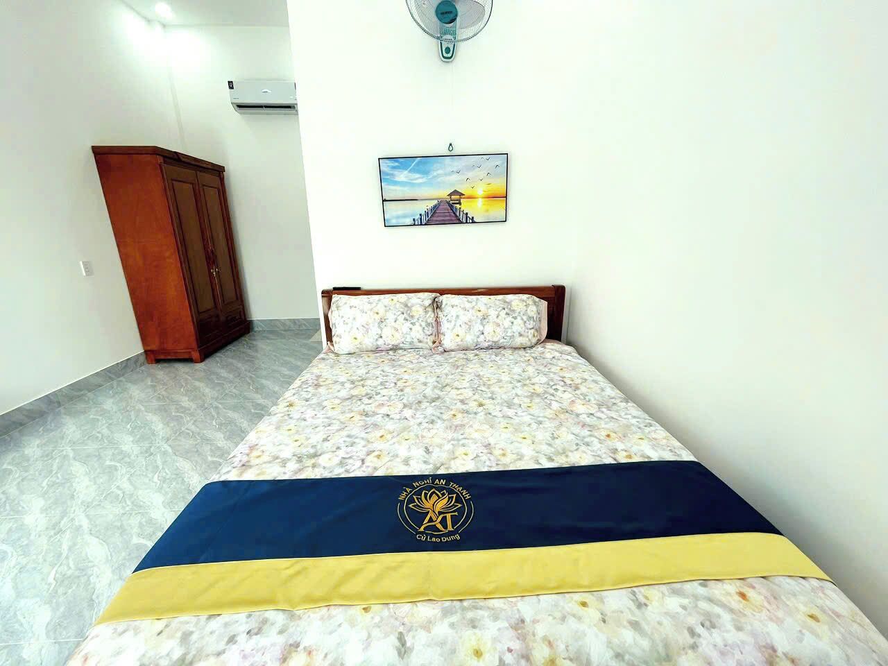 A bedroom with a bed, a wooden wardrobe, a wall-mounted air conditioner, and a framed picture.