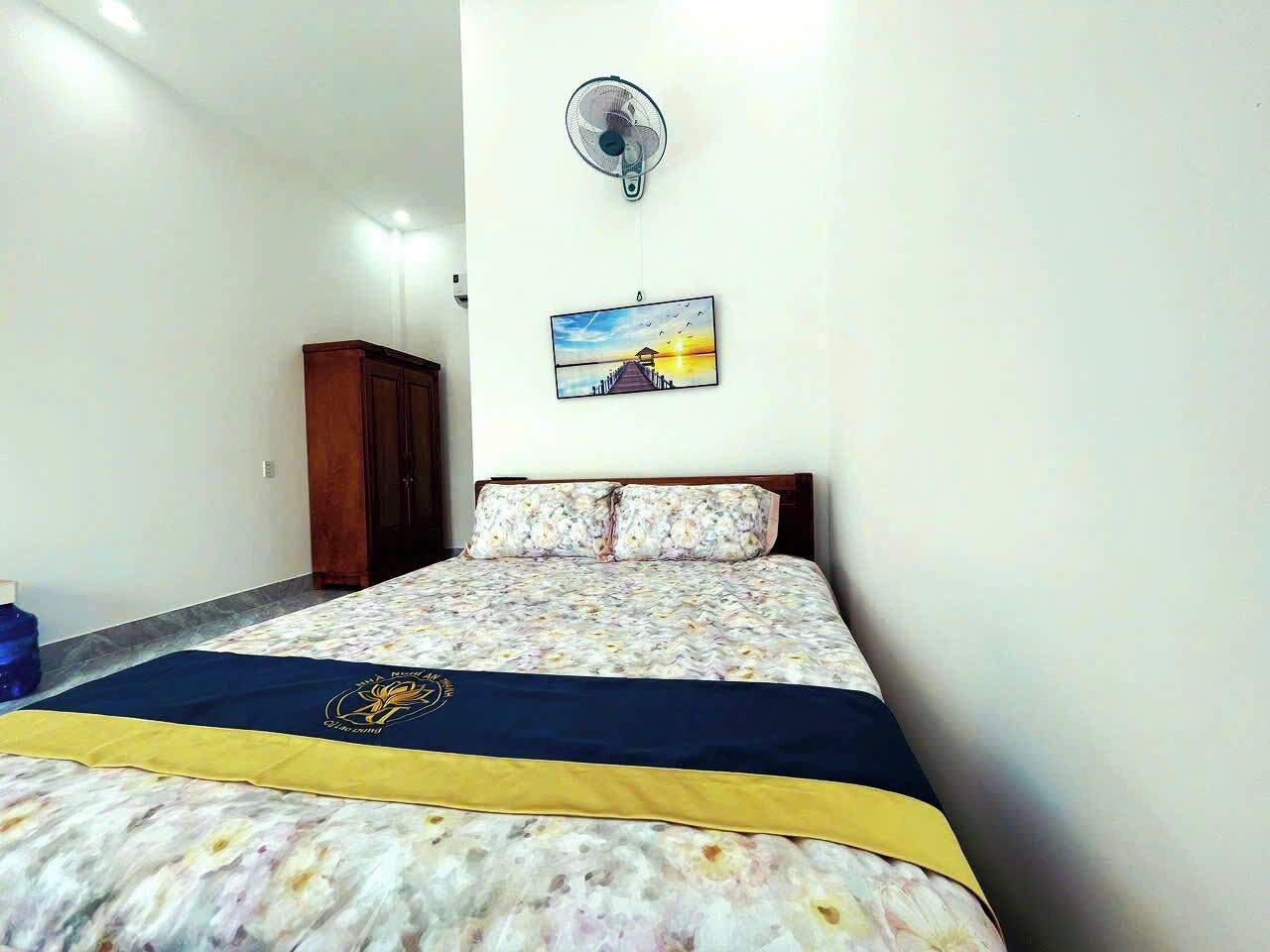 Un dormitorio con cama, un ventilador de pared, un cuadro y un armario de madera.