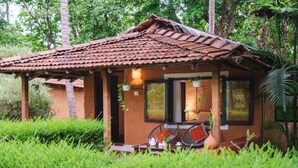 A small, rustic building with a tiled roof, a porch with chairs, and a table set for dining. - Natures Nest Goa (Sanguem)