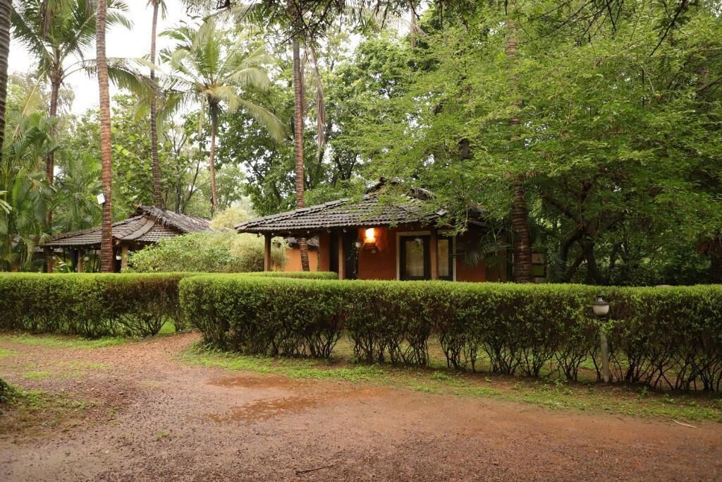 A rustic building with a tiled roof, surrounded by lush greenery and a well-maintained hedge.