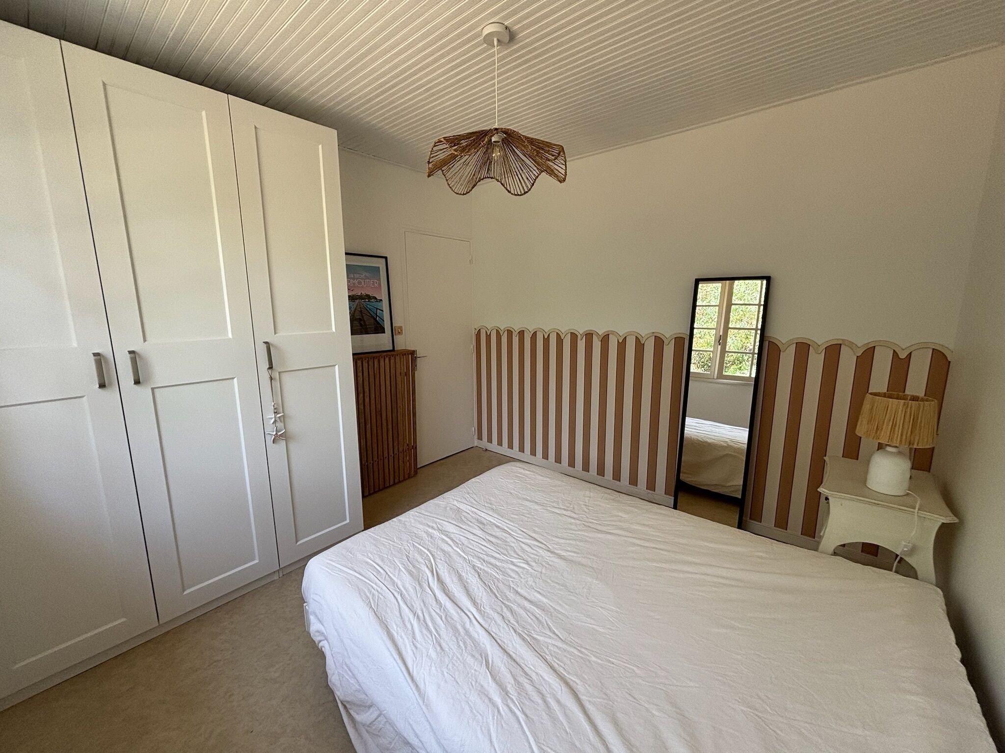 Een slaapkamer met een bed, een kledingkast, een radiator, een spiegel en een hanglamp.