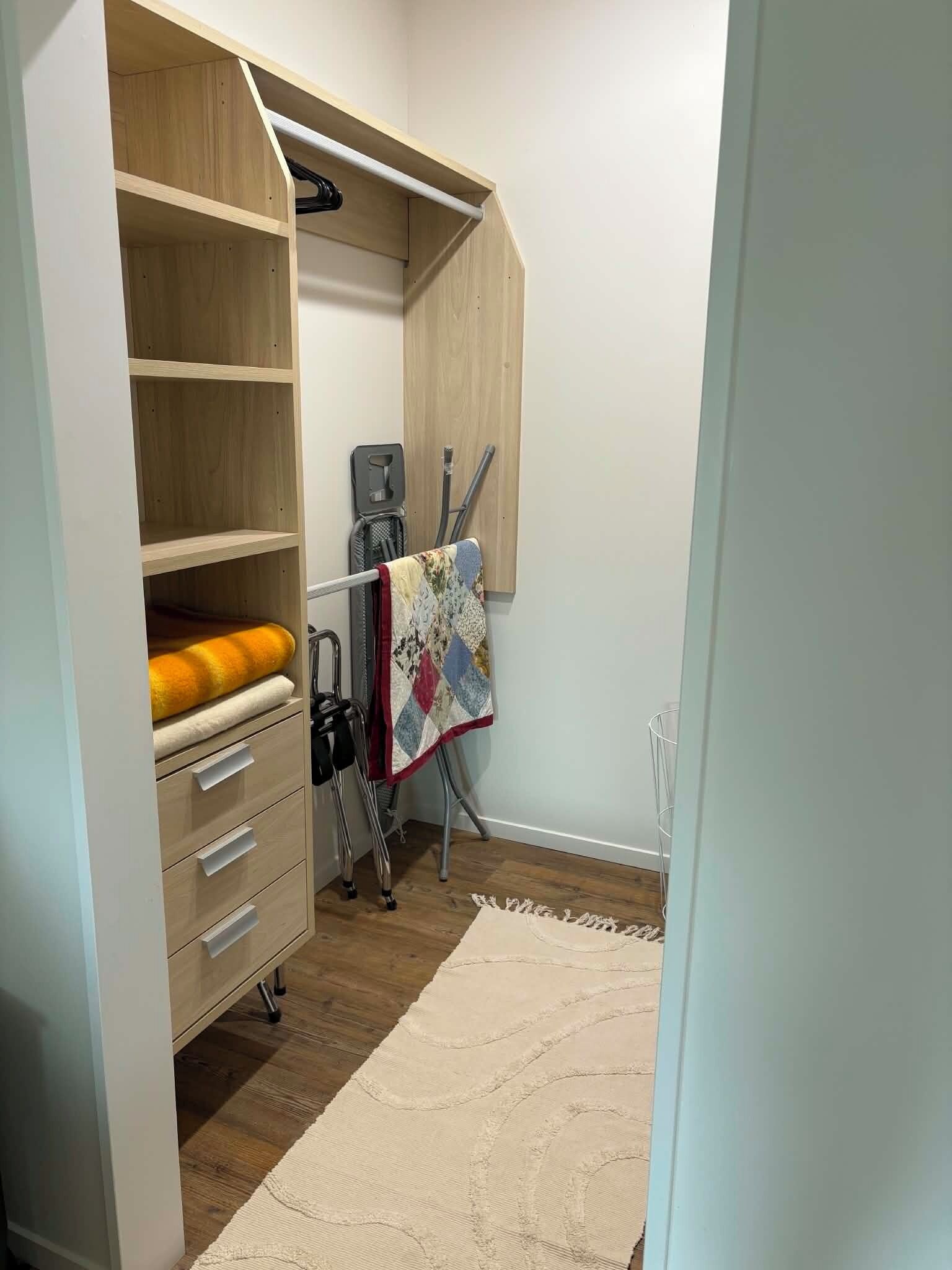 A walk-in closet with open shelves, a hanging rack, and a vacuum cleaner.