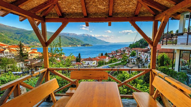 Un tavolo e panche di legno sotto un tetto di paglia, con vista su un lago e una cittadina.