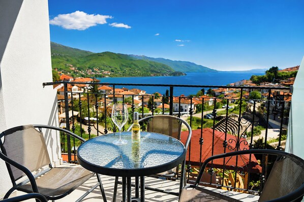 Ein Balkon mit Tisch und Stühlen, einer Weinflasche und Blick auf einen See und Berge.