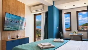 Una camera d'albergo con un letto, una televisione, una scrivania con una sedia e vista sul mare.