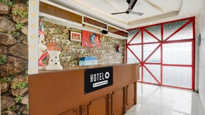 Een hotel receptiebalie met een stenen achtergrond, een 'HOTELO' bord en een groot raam met rode lijst.