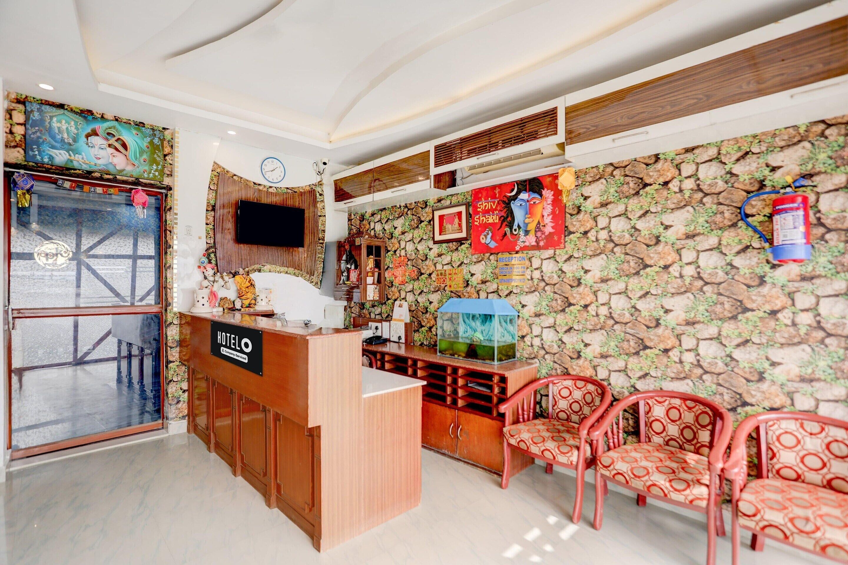 A hotel reception area with a wooden counter, a television mounted on the wall, and a stone wall with a floral pattern.