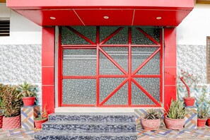 A building entrance with a red-framed window, potted plants, and a patterned tile floor.