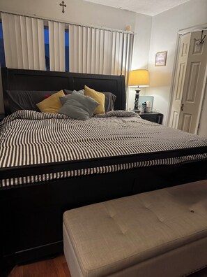 Ein Schlafzimmer mit einem Bett, einem Nachttisch, einer Lampe und einer Tür.