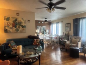 Ein Wohnzimmer mit einem blauen Sofa, einem Glastisch und einem Essbereich mit weißen Stühlen.
