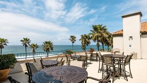 A terrace with outdoor seating, a view of the sea, and palm trees. - Unwind In Premium Beach-front Resort with Panoramic Ocean Views. 1Bd w/ Balcony (Carlsbad)
