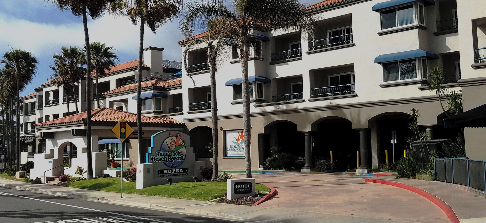 A multi-story hotel with a sign for Tamarack Beach Resort, featuring a registration area and a clear driveway.