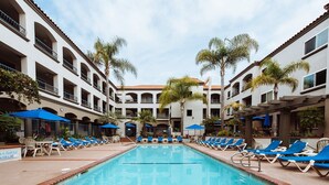 A pool area with lounge chairs and umbrellas, surrounded by multi-story buildings with balconies. - Unwind In Premium Beach-front Resort with Panoramic Ocean Views. 1Bd w/ Balcony (Carlsbad)