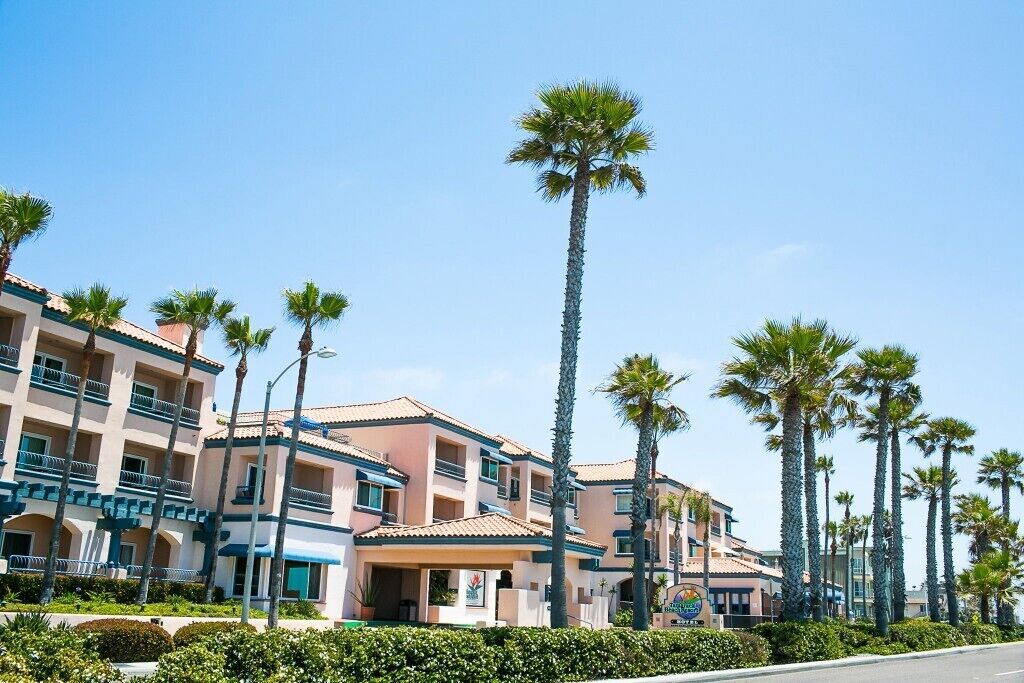 A multi-story hotel with balconies, palm trees, and a clear blue sky.