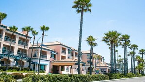 A multi-story hotel with balconies, palm trees, and a clear blue sky. - Unwind In Premium Beach-front Resort with Panoramic Ocean Views. 1Bd w/ Balcony (Carlsbad)